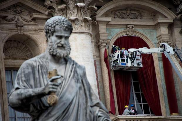 Trabalhadores penduram cortinas vermelhas na Basílica de São Pedro Johannes Eisele/AFP